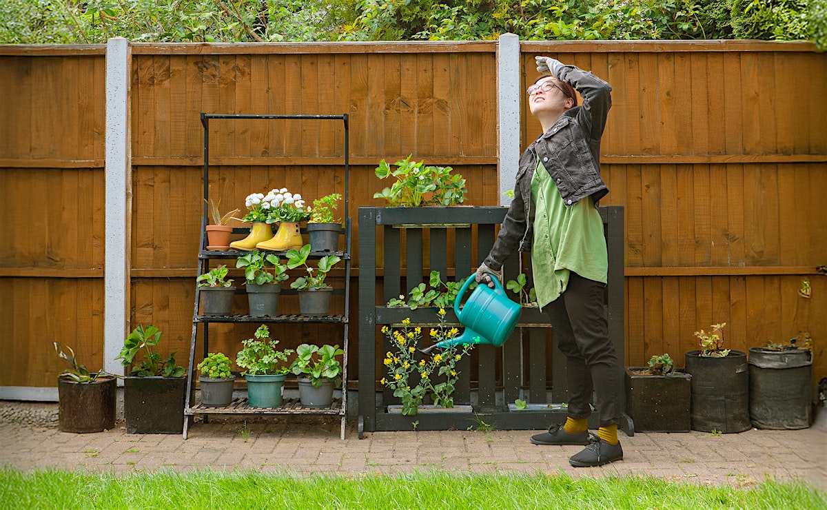 Performer watering plants in a garden looking up at the sky